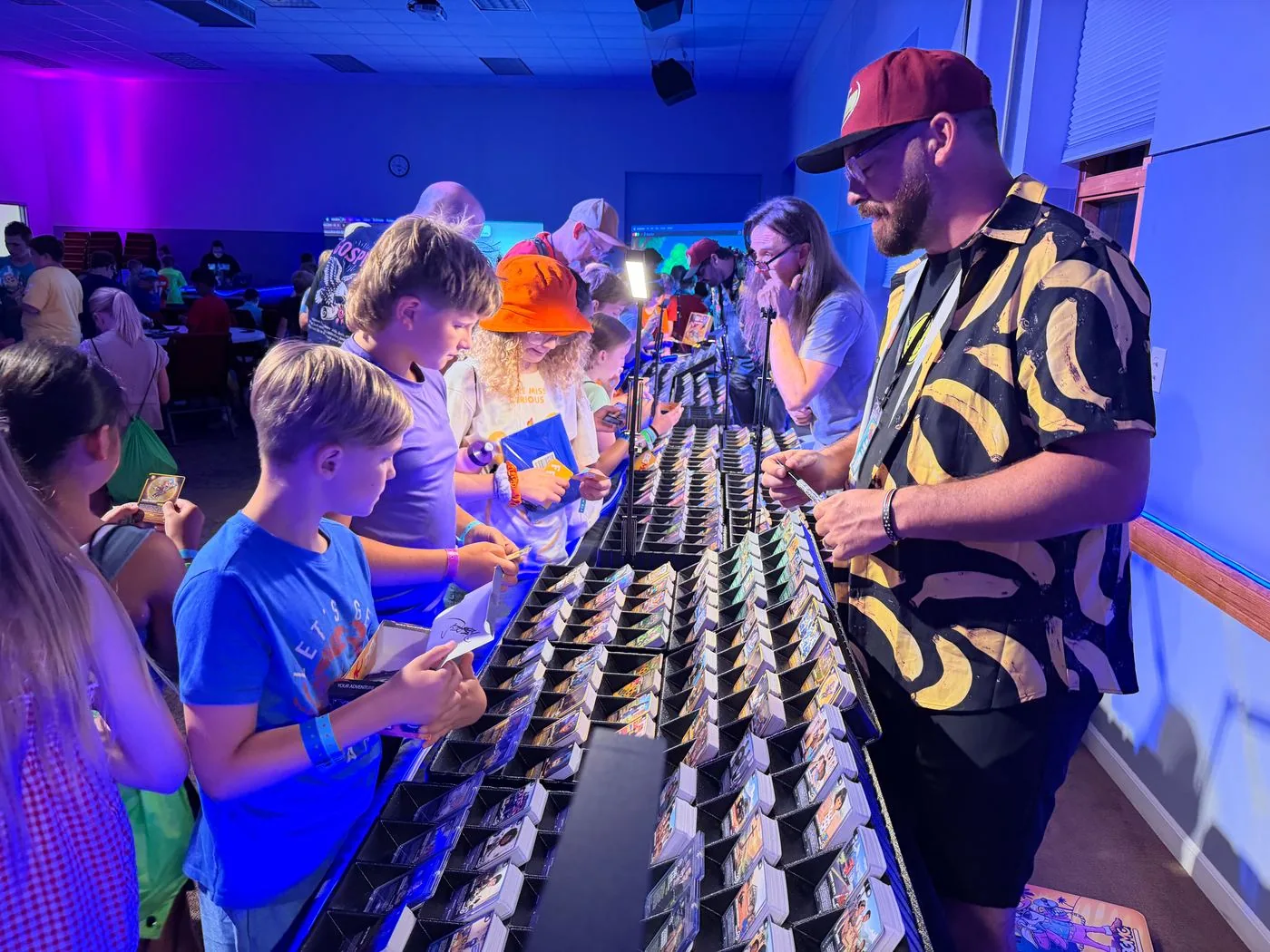 Children browse rows of BGMC cards with a team member at an event table.
